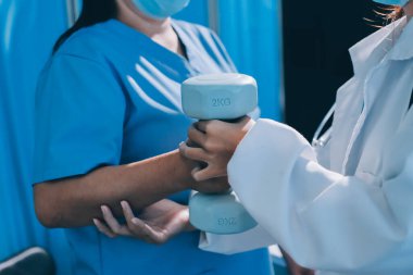 Evde oturma odasında terapi ve rehabilitasyon görürken, bakıcı ya da fizyoterapist yaşlılara yardım ederken, son sınıf öğrencisi olan Asyalı bir kadın ya da hemşire kol egzersizi için halteri kaldırıyor..