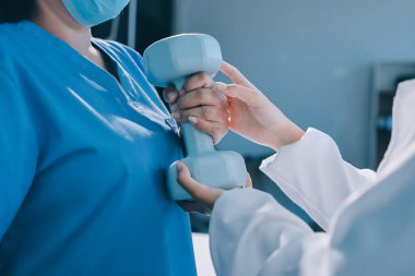 Evde oturma odasında terapi ve rehabilitasyon görürken, bakıcı ya da fizyoterapist yaşlılara yardım ederken, son sınıf öğrencisi olan Asyalı bir kadın ya da hemşire kol egzersizi için halteri kaldırıyor..