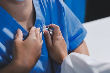 Ev bakımı hemşiresi ve yaşlılar kardiyoloji sağlık hizmetleri. Genç İspanyol kadın doktor hemşirenin yakın çekimleri sırasında steteskop kullanarak olgun beyaz hasta kalp atışlarını kontrol et.