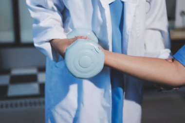 Evde oturma odasında terapi ve rehabilitasyon görürken, bakıcı ya da fizyoterapist yaşlılara yardım ederken, son sınıf öğrencisi olan Asyalı bir kadın ya da hemşire kol egzersizi için halteri kaldırıyor..