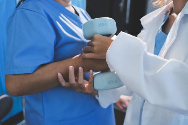 Evde oturma odasında terapi ve rehabilitasyon görürken, bakıcı ya da fizyoterapist yaşlılara yardım ederken, son sınıf öğrencisi olan Asyalı bir kadın ya da hemşire kol egzersizi için halteri kaldırıyor..