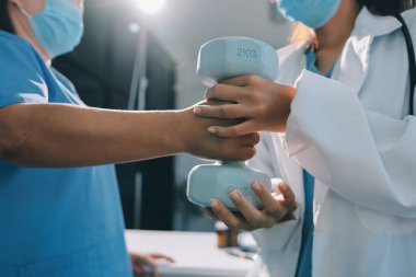 Evde oturma odasında terapi ve rehabilitasyon görürken, bakıcı ya da fizyoterapist yaşlılara yardım ederken, son sınıf öğrencisi olan Asyalı bir kadın ya da hemşire kol egzersizi için halteri kaldırıyor..