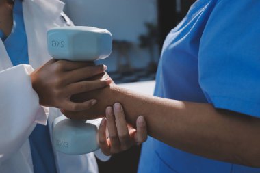 Evde oturma odasında terapi ve rehabilitasyon görürken, bakıcı ya da fizyoterapist yaşlılara yardım ederken, son sınıf öğrencisi olan Asyalı bir kadın ya da hemşire kol egzersizi için halteri kaldırıyor..