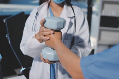 Evde oturma odasında terapi ve rehabilitasyon görürken, bakıcı ya da fizyoterapist yaşlılara yardım ederken, son sınıf öğrencisi olan Asyalı bir kadın ya da hemşire kol egzersizi için halteri kaldırıyor..