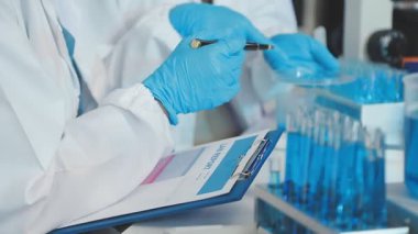 Bilim adamı deney tüpü tutuyor ve laboratuvar üzerinde çalışıyor.