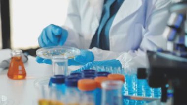 Laboratuvar önlüklü bilim adamı deney tüpü tutuyor ve mikroskoba bakıyor.