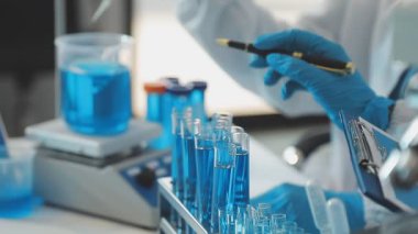 Koruyucu gözlüklü bilim adamı elinde sıvı test tüpleri tutuyor.