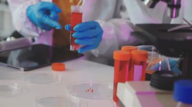 Tıbbi eldivenli bir laboratuvar asistanı elinde bir test tüpü tutuyor.