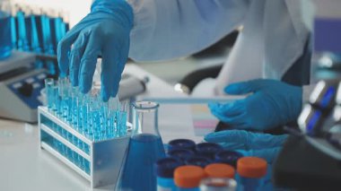 Laboratuvar önlüklü ve koruyucu eldivenli bir bilim adamı laboratuarda sıvı tüpleri tutuyor.