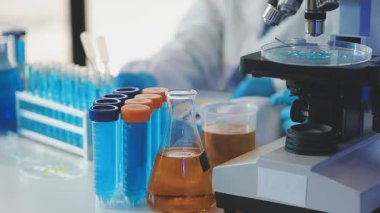 Bir laboratuvar arka planında sıvı ve mikroskop bulunan bir test tüpünün yakın plan görüntüsü.