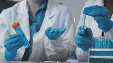 Laboratuvar önlüklü bilim adamı elinde sıvı tüpler tutuyor.