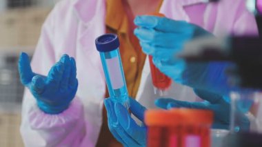 Koruyucu eldivenler giymiş bilim adamı elinde bir deney tüpü tutuyor.