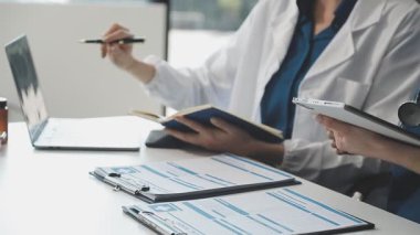 Doktorlar, modern ofisteki masada hastalarla tartışıyor ve tıbbi rapor yazıyorlar.