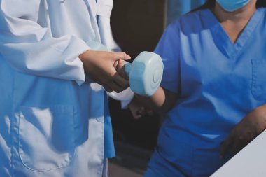 Evde oturma odasında terapi ve rehabilitasyon görürken, bakıcı ya da fizyoterapist yaşlılara yardım ederken, son sınıf öğrencisi olan Asyalı bir kadın ya da hemşire kol egzersizi için halteri kaldırıyor..