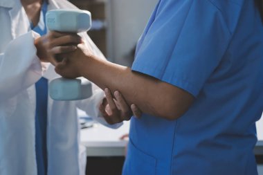 Evde oturma odasında terapi ve rehabilitasyon görürken, bakıcı ya da fizyoterapist yaşlılara yardım ederken, son sınıf öğrencisi olan Asyalı bir kadın ya da hemşire kol egzersizi için halteri kaldırıyor..