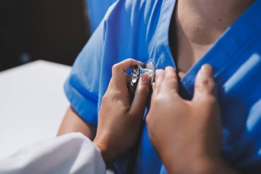 Ev bakımı hemşiresi ve yaşlılar kardiyoloji sağlık hizmetleri. Genç İspanyol kadın doktor hemşirenin yakın çekimleri sırasında steteskop kullanarak olgun beyaz hasta kalp atışlarını kontrol et.