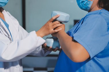 Evde oturma odasında terapi ve rehabilitasyon görürken, bakıcı ya da fizyoterapist yaşlılara yardım ederken, son sınıf öğrencisi olan Asyalı bir kadın ya da hemşire kol egzersizi için halteri kaldırıyor..