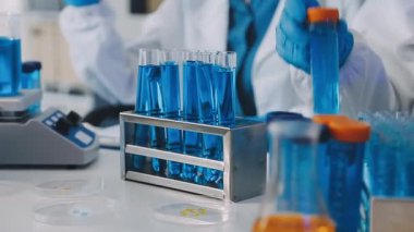 Bilim adamı elinde bardakta sıvı olan bir test tüpü tutuyor.