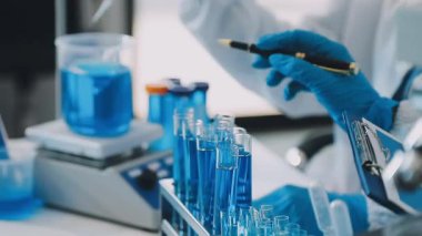 Koruyucu eldivenli ve gözlüklü bir bilim adamı elinde kanla test tüpleri tutuyor.