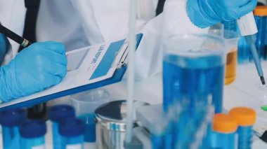 Koruyucu eldivenli bilim adamı laboratuarda cam tüpler ve test tüpleri tutuyor.