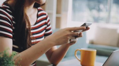 Genç Asyalı kız elinde akıllı bir telefon tutuyor ve kafede çalışırken cep telefonu kullanıyor.