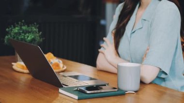 Laptop kullanan ve kafede çalışırken sıcak kahve içen genç bir kadın.