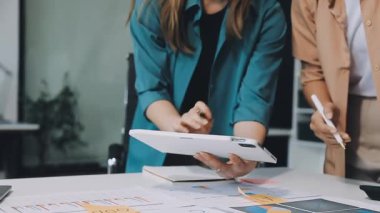 Genç bayan tasarımcı dijital tablet kullanıyor ve ofisteki meslektaşının çizelgesine işaret ediyor..