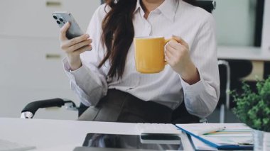 Genç iş kadını elinde akıllı bir telefonla kahveye bakıyor.