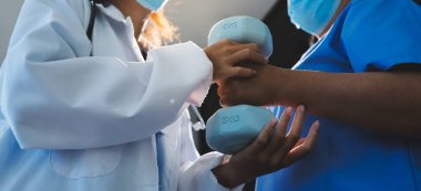 Evde oturma odasında terapi ve rehabilitasyon görürken, bakıcı ya da fizyoterapist yaşlılara yardım ederken, son sınıf öğrencisi olan Asyalı bir kadın ya da hemşire kol egzersizi için halteri kaldırıyor..