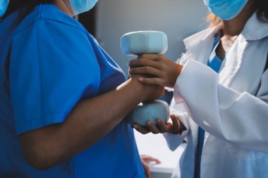 Evde oturma odasında terapi ve rehabilitasyon görürken, bakıcı ya da fizyoterapist yaşlılara yardım ederken, son sınıf öğrencisi olan Asyalı bir kadın ya da hemşire kol egzersizi için halteri kaldırıyor..