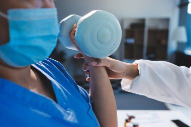 Evde oturma odasında terapi ve rehabilitasyon görürken, bakıcı ya da fizyoterapist yaşlılara yardım ederken, son sınıf öğrencisi olan Asyalı bir kadın ya da hemşire kol egzersizi için halteri kaldırıyor..