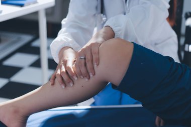 Kadın doktor elleri, erkek bir hastanın bacağını ve dizini uzatarak fizik tedavi uyguluyor.