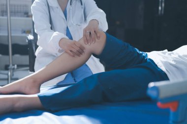 Kadın doktor elleri, erkek bir hastanın bacağını ve dizini uzatarak fizik tedavi uyguluyor.