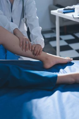 Kadın doktor elleri, erkek bir hastanın bacağını ve dizini uzatarak fizik tedavi uyguluyor.