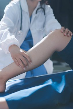Kadın doktor elleri, erkek bir hastanın bacağını ve dizini uzatarak fizik tedavi uyguluyor.