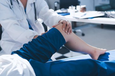 Kadın doktor elleri, erkek bir hastanın bacağını ve dizini uzatarak fizik tedavi uyguluyor.