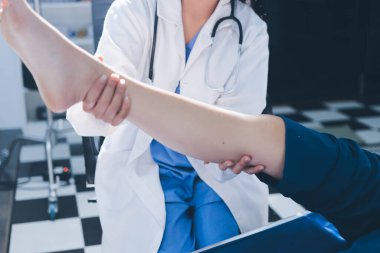 Kadın doktor elleri, erkek bir hastanın bacağını ve dizini uzatarak fizik tedavi uyguluyor.