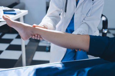 Kadın doktor elleri, erkek bir hastanın bacağını ve dizini uzatarak fizik tedavi uyguluyor.