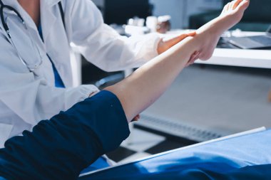 Kadın doktor elleri, erkek bir hastanın bacağını ve dizini uzatarak fizik tedavi uyguluyor.