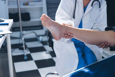 Kadın doktor elleri, erkek bir hastanın bacağını ve dizini uzatarak fizik tedavi uyguluyor.