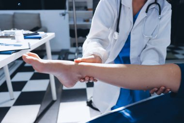 Kadın doktor elleri, erkek bir hastanın bacağını ve dizini uzatarak fizik tedavi uyguluyor.