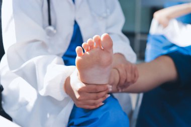 Kadın doktor elleri, erkek bir hastanın bacağını ve dizini uzatarak fizik tedavi uyguluyor.