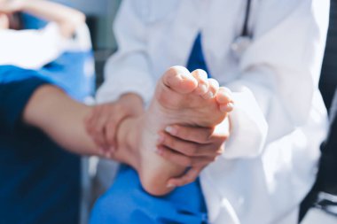 Kadın doktor elleri, erkek bir hastanın bacağını ve dizini uzatarak fizik tedavi uyguluyor.