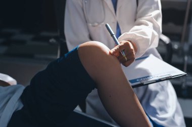 Kadın doktor elleri, erkek bir hastanın bacağını ve dizini uzatarak fizik tedavi uyguluyor.