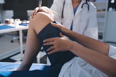 Kadın doktor elleri, erkek bir hastanın bacağını ve dizini uzatarak fizik tedavi uyguluyor.