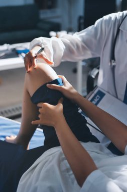 Kadın doktor elleri, erkek bir hastanın bacağını ve dizini uzatarak fizik tedavi uyguluyor.