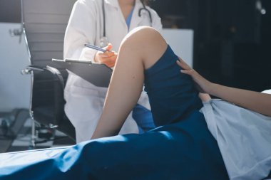 Kadın doktor elleri, erkek bir hastanın bacağını ve dizini uzatarak fizik tedavi uyguluyor.