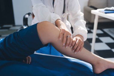 Kadın doktor elleri, erkek bir hastanın bacağını ve dizini uzatarak fizik tedavi uyguluyor.