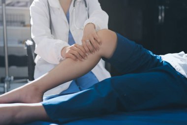 Kadın doktor elleri, erkek bir hastanın bacağını ve dizini uzatarak fizik tedavi uyguluyor.