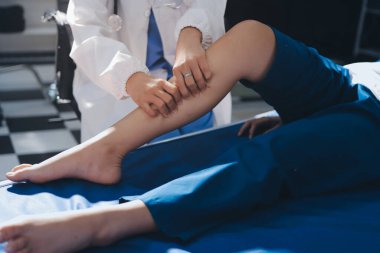 Kadın doktor elleri, erkek bir hastanın bacağını ve dizini uzatarak fizik tedavi uyguluyor.